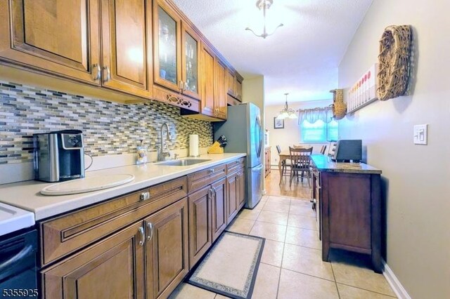 kitchen with a sink, backsplash, brown cabinetry, and freestanding refrigerator