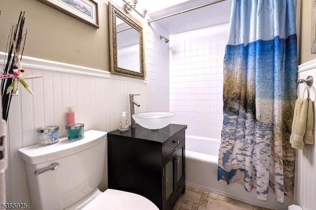 bathroom with a wainscoted wall, shower / bath combination with curtain, toilet, and vanity