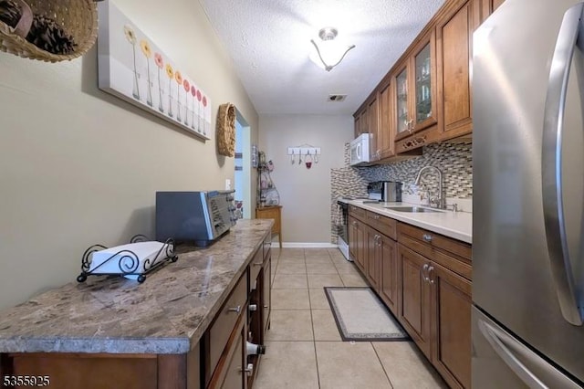 kitchen with freestanding refrigerator, a sink, white microwave, brown cabinets, and range with electric cooktop