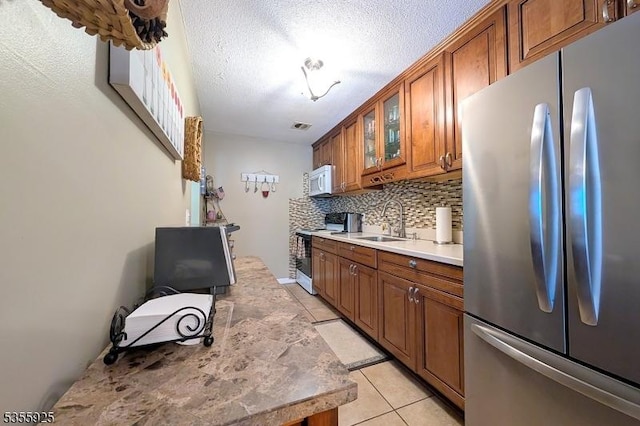 kitchen with freestanding refrigerator, range with electric stovetop, a sink, brown cabinetry, and light tile patterned floors