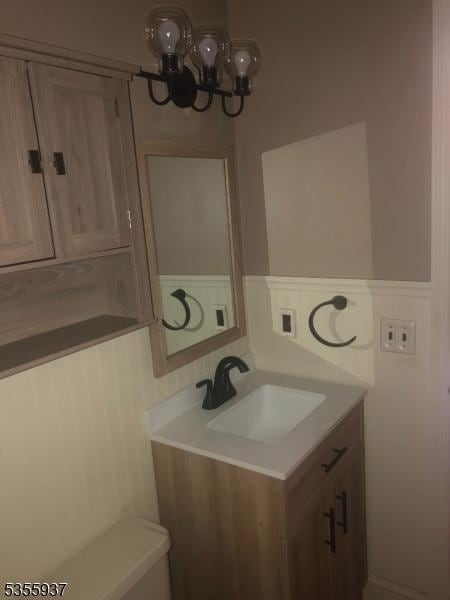 half bath featuring a chandelier, vanity, and toilet