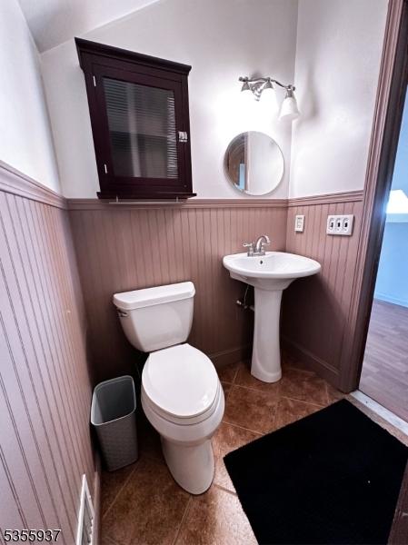 bathroom with wainscoting, toilet, tile patterned floors, and a sink