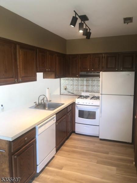 kitchen featuring white appliances, a sink, under cabinet range hood, light countertops, and dark brown cabinets