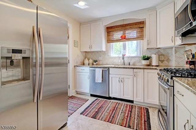kitchen with appliances with stainless steel finishes, white cabinets, backsplash, light stone countertops, and a sink