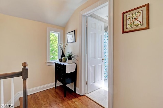 hallway featuring wood finished floors, vaulted ceiling, and baseboards