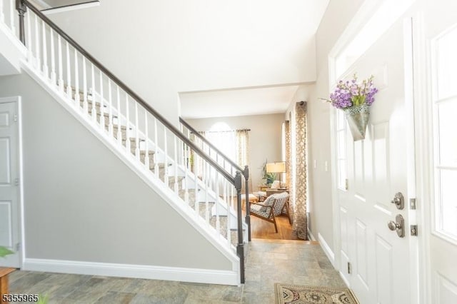 foyer entrance featuring stairs, baseboards, and stone finish floors