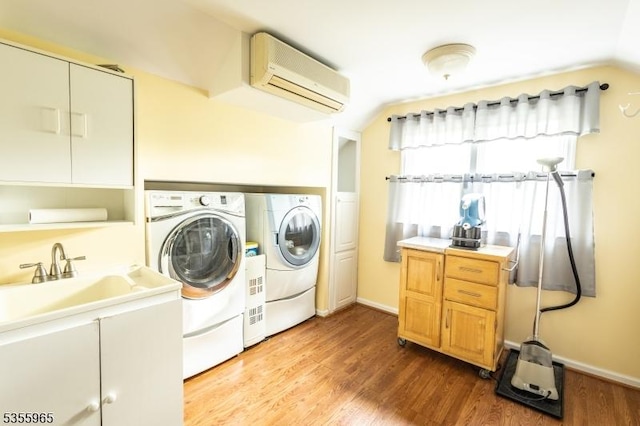 laundry room featuring washing machine and clothes dryer, a wall mounted AC, wood finished floors, and baseboards
