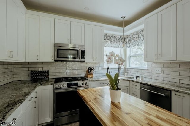 kitchen with butcher block countertops, stainless steel appliances, a sink, white cabinets, and backsplash