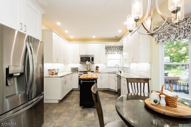 kitchen with appliances with stainless steel finishes, a chandelier, white cabinets, backsplash, and a center island