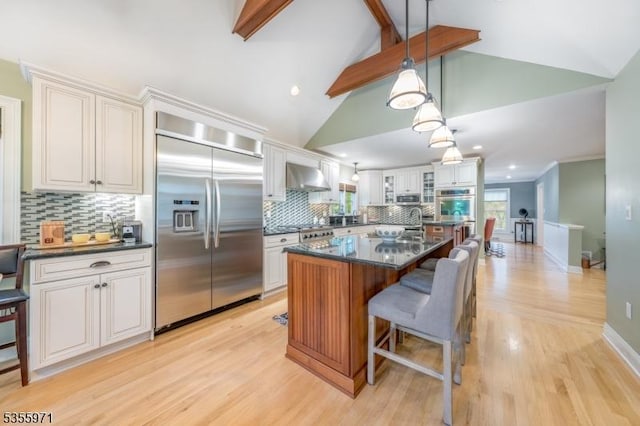 kitchen with appliances with stainless steel finishes, wall chimney exhaust hood, dark countertops, glass insert cabinets, and recessed lighting