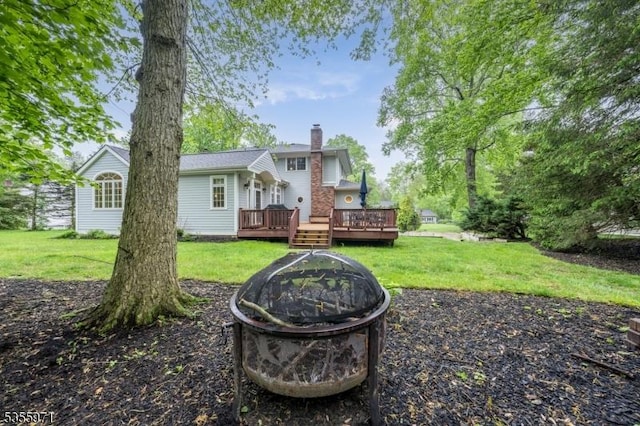 back of house with an outdoor fire pit, a chimney, a lawn, and a deck