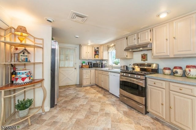 kitchen with appliances with stainless steel finishes, under cabinet range hood, stone finish flooring, light countertops, and glass insert cabinets