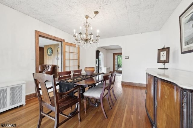 10 Highland Pl, West Orange Twp, NJ 07052 - dining room featuring radiator, arched walkways, a chandelier, wood-type flooring, and baseboards