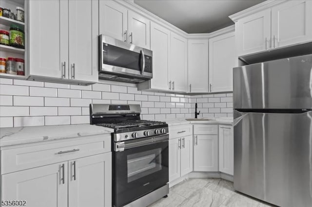 kitchen featuring stainless steel appliances, a sink, white cabinetry, light stone counters, and light marble finish floors