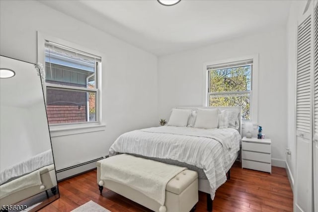 bedroom with a baseboard heating unit, wood finished floors, and a closet