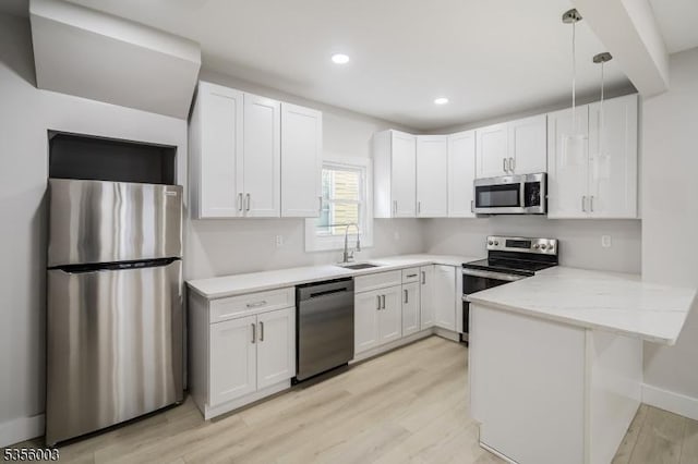 kitchen featuring stainless steel appliances, a sink, a peninsula, light wood-style floors, and white cabinetry