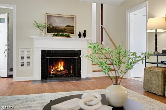 living area with a tiled fireplace, baseboards, visible vents, and wood finished floors