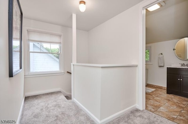 hall with light carpet, baseboards, and a sink