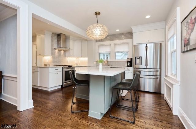 kitchen with stainless steel appliances, wall chimney range hood, a breakfast bar area, white cabinetry, and recessed lighting