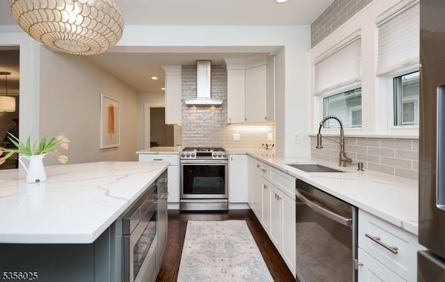 kitchen featuring wall chimney range hood, appliances with stainless steel finishes, a sink, dark wood-style flooring, and decorative backsplash