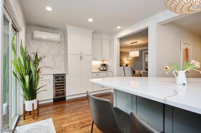 kitchen featuring wine cooler, a wall unit AC, wood finished floors, white cabinetry, and light stone counters
