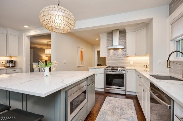 kitchen with stainless steel appliances, wall chimney exhaust hood, a sink, dark wood finished floors, and white cabinets