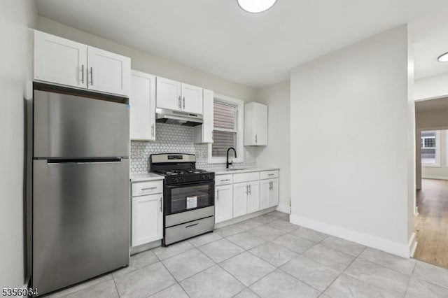 kitchen with appliances with stainless steel finishes, under cabinet range hood, light countertops, white cabinetry, and backsplash