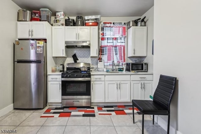 kitchen with appliances with stainless steel finishes, under cabinet range hood, a sink, and tasteful backsplash