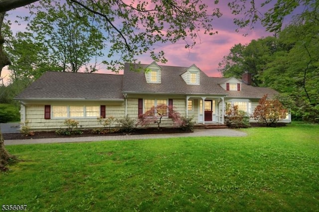 new england style home with a front yard, a chimney, and a porch