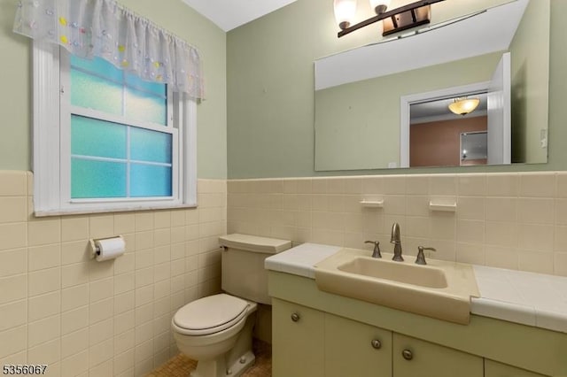 half bath featuring toilet, tile walls, vanity, and wainscoting