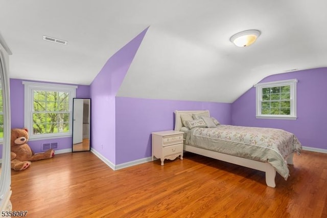 bedroom featuring vaulted ceiling, light wood-style floors, baseboards, and multiple windows