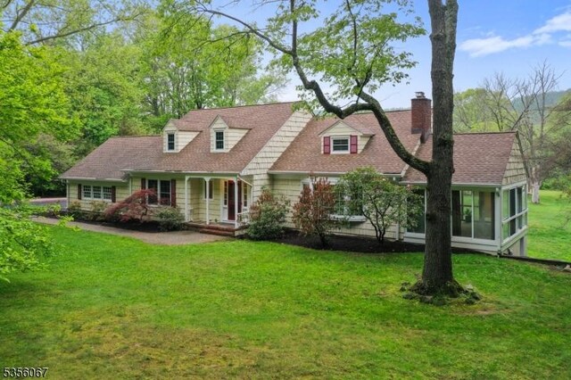 cape cod-style house with a chimney, a sunroom, a front yard, and covered porch