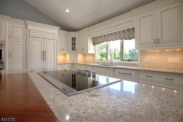 kitchen featuring a sink, black electric stovetop, vaulted ceiling, tasteful backsplash, and light stone countertops