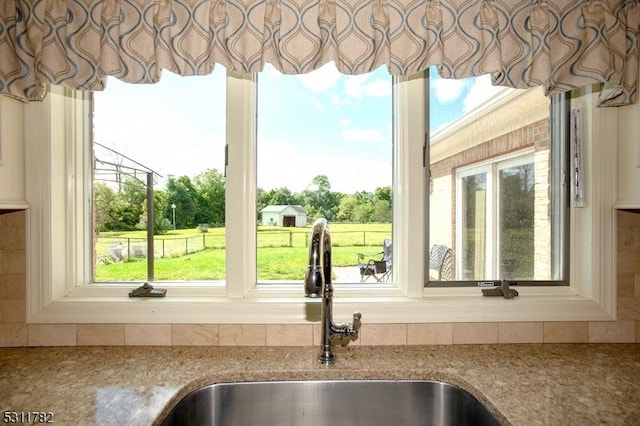 kitchen view of a sink, decorative backsplash, and light stone counters