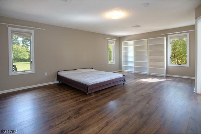 bedroom with multiple windows, dark wood finished floors, and baseboards