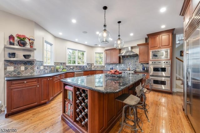 kitchen with open shelves, appliances with stainless steel finishes, wall chimney range hood, a center island, and a kitchen breakfast bar
