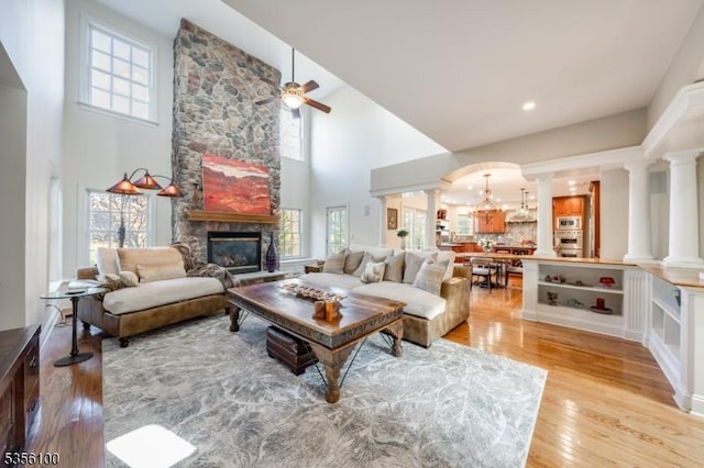 living room featuring a towering ceiling, plenty of natural light, light wood finished floors, a fireplace, and a ceiling fan