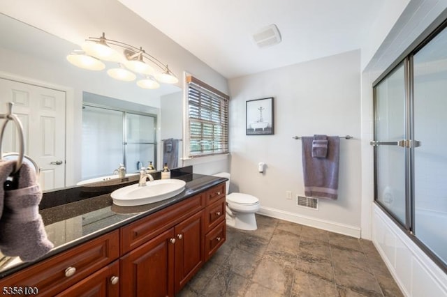 full bath featuring vanity, toilet, baseboards, stone finish flooring, and bath / shower combo with glass door