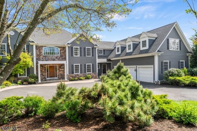 view of front of home with driveway, stone siding, roof with shingles, and a garage
