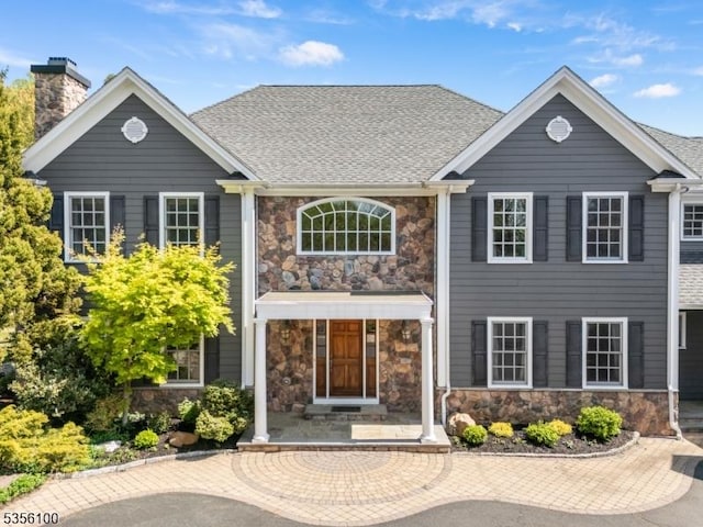 view of front of property with stone siding, a chimney, and a shingled roof