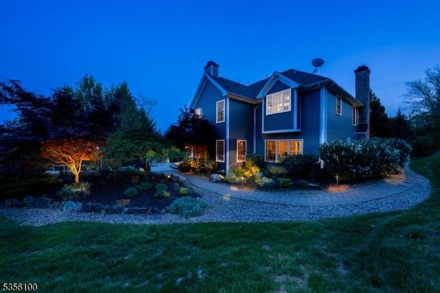 property exterior at dusk featuring a chimney and a lawn
