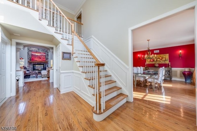 staircase featuring wood finished floors, a decorative wall, ornamental molding, a stone fireplace, and wainscoting