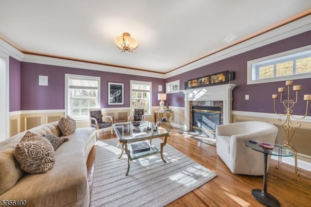 living area featuring crown molding, wainscoting, a premium fireplace, and wood finished floors
