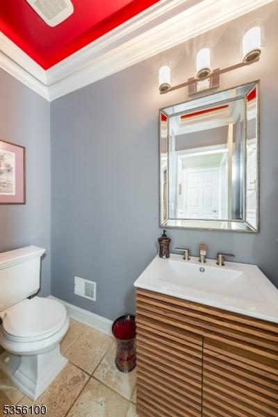 half bathroom featuring toilet, tile patterned flooring, crown molding, vanity, and baseboards