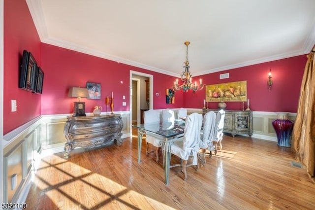 dining space featuring a chandelier, crown molding, wood finished floors, wainscoting, and a decorative wall