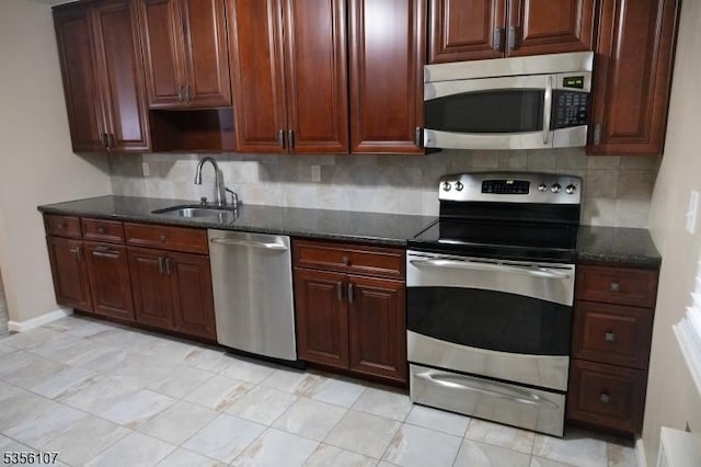 kitchen with stainless steel appliances, a sink, backsplash, and dark stone countertops