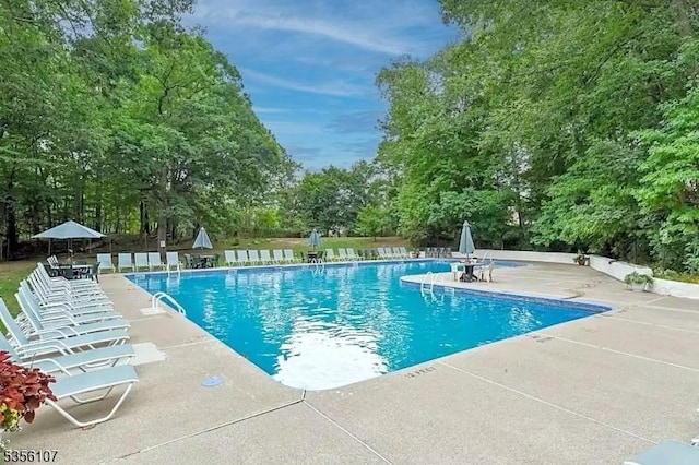community pool with a patio, view of scattered trees, and fence