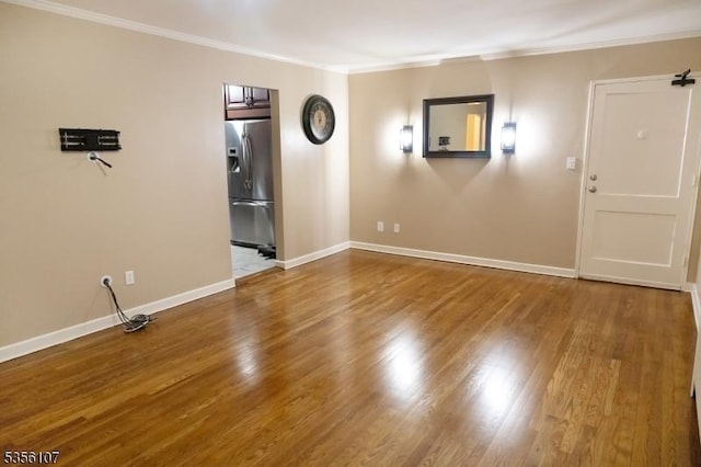 empty room featuring crown molding, baseboards, and wood finished floors