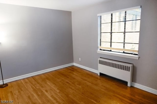 empty room featuring radiator heating unit, baseboards, and wood finished floors