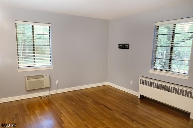 empty room featuring radiator heating unit, a wall mounted air conditioner, healthy amount of natural light, and wood finished floors